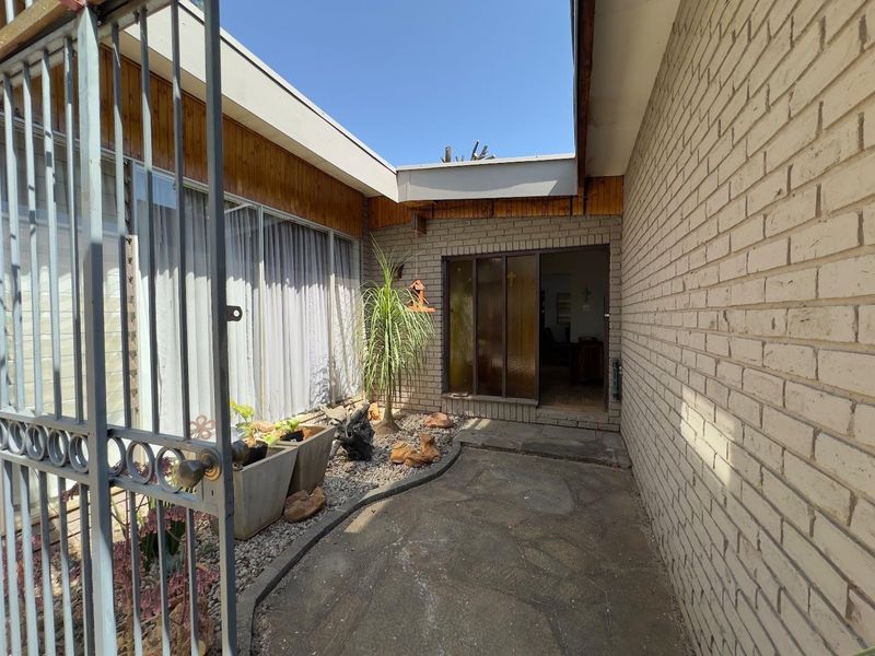 A private entrance courtyard featuring a stone paved walkway, brick walls, and a secure metal gate leading to the main sliding glass door.