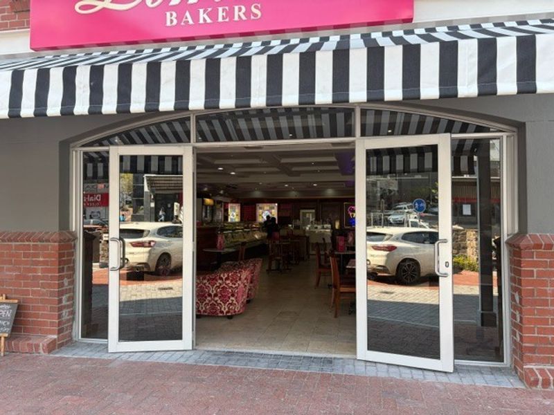 Front entrance of a retail bakery featuring a striped awning, glass double doors, and brick exterior detailing.