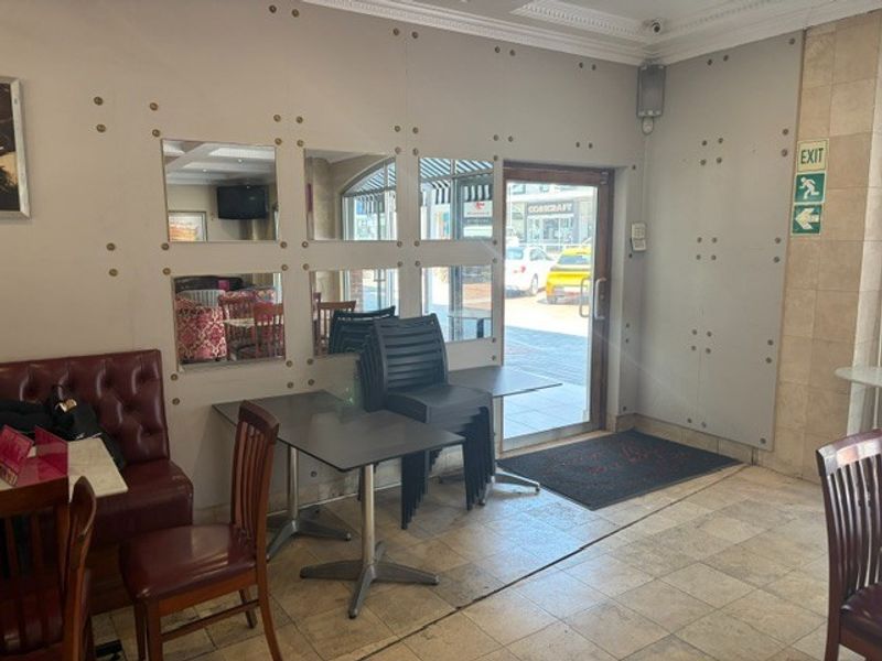 Entrance area of a retail space featuring tiled flooring, decorative wall paneling with inset mirrors, and a glass door leading to the street.