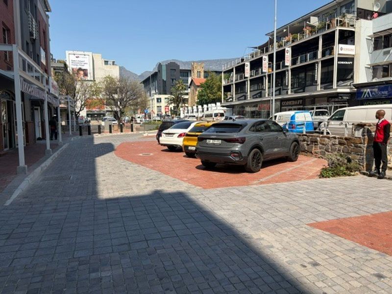 A street-level view of a commercial retail area featuring paved parking spaces and surrounding multi-story building facades.