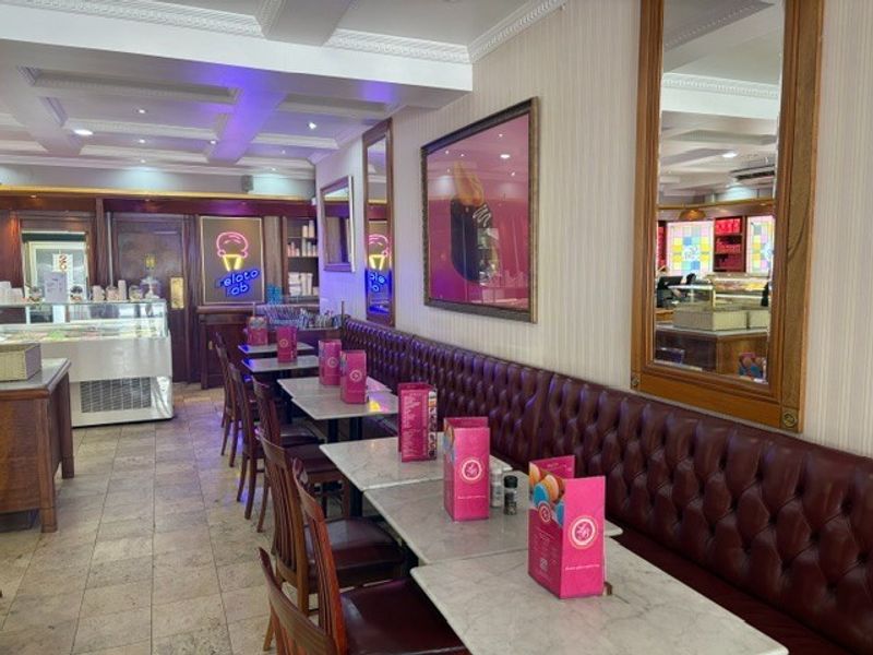 A well-maintained retail space featuring built-in leather banquette seating, decorative ceiling molding, recessed lighting, and tiled flooring, suitable for a cafe or restaurant.