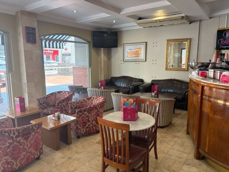 A retail seating area featuring tiled flooring, coffered ceilings with recessed lighting, and a large display window overlooking the street.