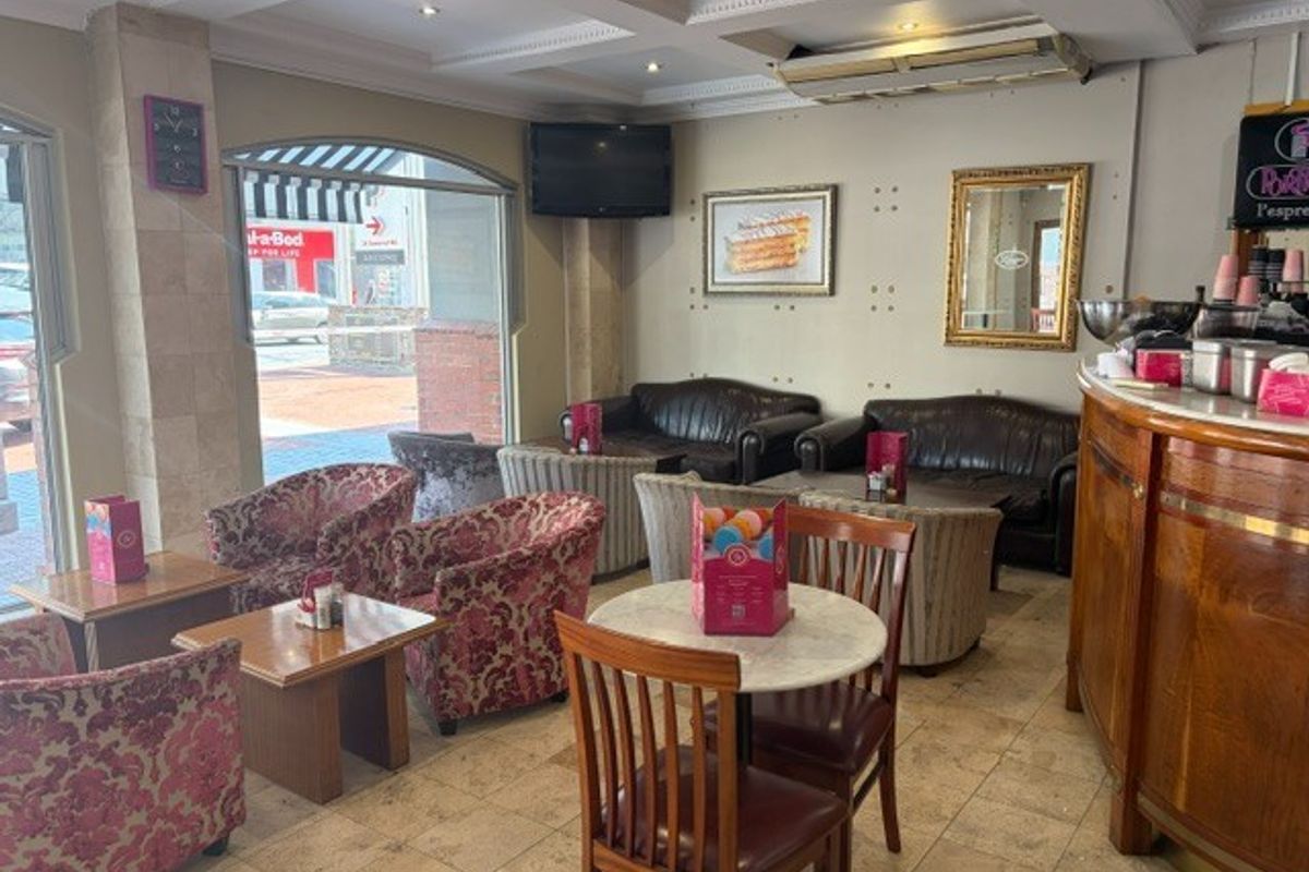 A retail seating area featuring tiled flooring, coffered ceilings with recessed lighting, and a large display window overlooking the street.