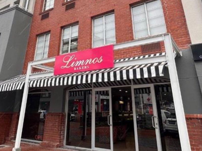 Street-level view of a retail storefront featuring a classic brick facade, striped awning, and large glass entrance doors.
