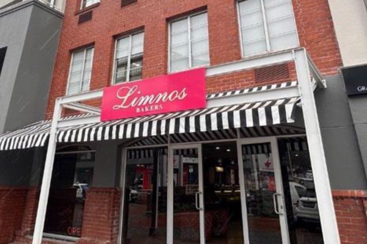Street-level view of a retail storefront featuring a classic brick facade, striped awning, and large glass entrance doors.