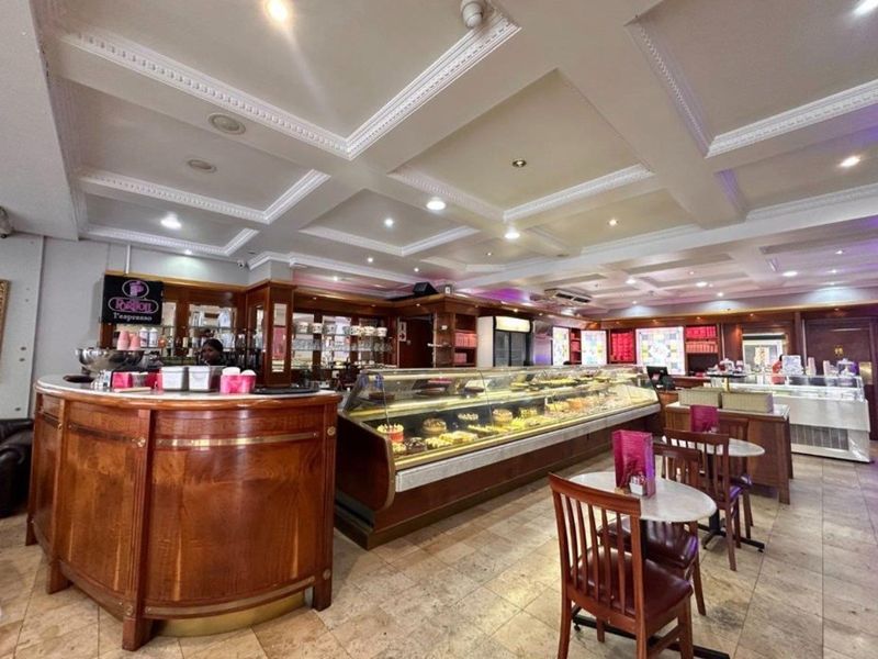 A well-maintained retail cafe space featuring a classic wooden service counter, extensive glass display cases, and an elegant coffered ceiling with recessed lighting.