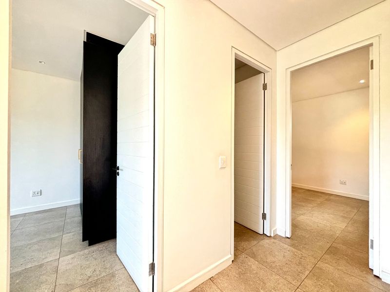 A bright, modern hallway featuring neutral tiled flooring, clean white walls, and access to multiple rooms with built-in storage cabinetry.