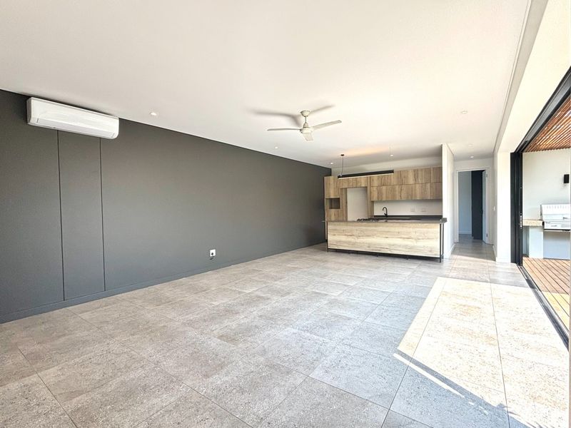 Spacious open-plan living area featuring modern kitchen cabinetry, tiled flooring, ceiling fan, and seamless access to an outdoor patio through large sliding glass doors.