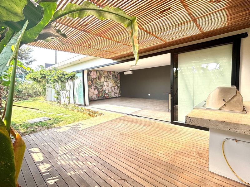 Spacious covered patio featuring timber decking, a built-in barbecue, and large sliding doors opening into an expansive, modern open-plan living area.
