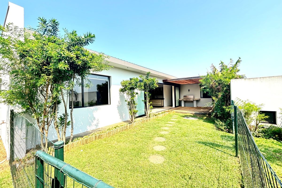 A well-maintained rear garden featuring a wooden deck, built-in braai area, and direct access to the interior through sliding doors.