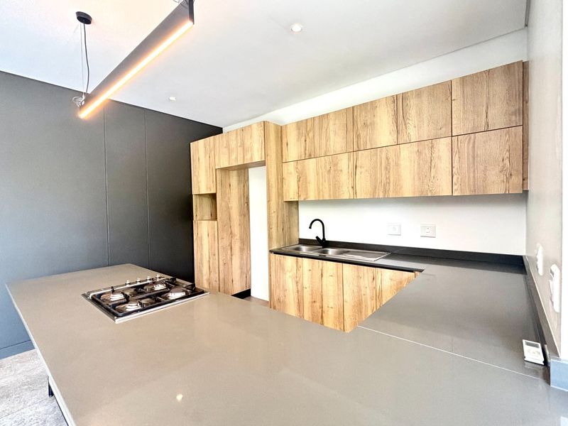 Modern kitchen featuring wood-grain cabinetry, sleek stone countertops, a built-in gas hob, and a contemporary black faucet.