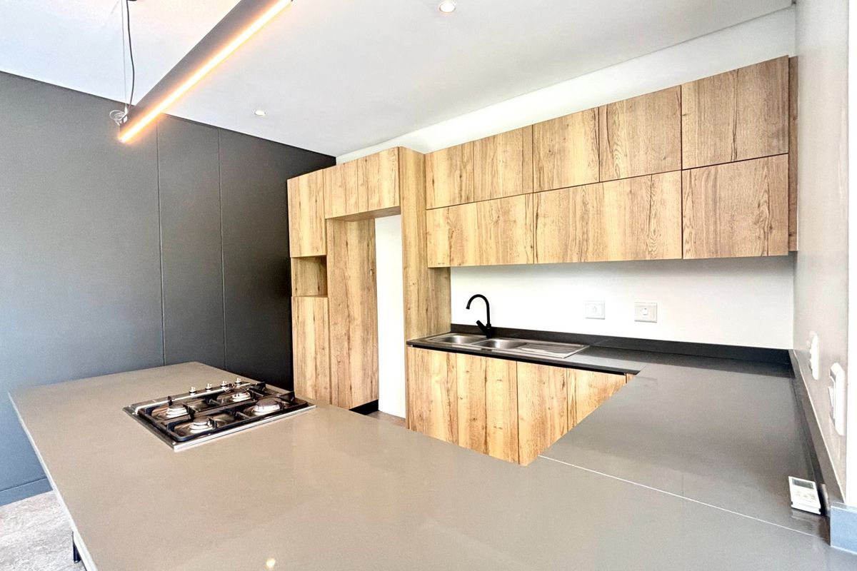 Modern kitchen featuring wood-grain cabinetry, sleek stone countertops, a built-in gas hob, and a contemporary black faucet.