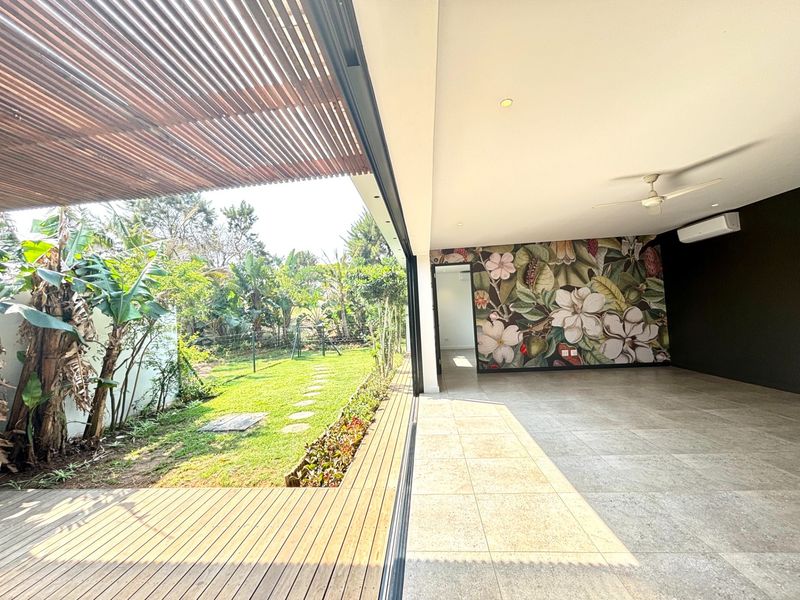 Spacious open-plan living area featuring large sliding glass doors that open onto a timber deck and garden, complete with ceiling fan and air conditioning.