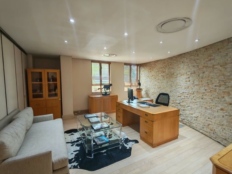 A professional office space featuring a textured stone feature wall, recessed ceiling lighting, and light wood flooring, creating a warm and functional work environment.