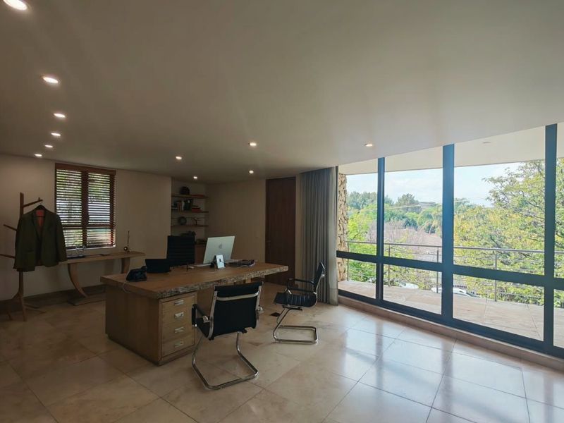 A spacious, well-lit office featuring stone tile flooring, built-in shelving, and expansive windows providing natural light and access to an outdoor balcony.