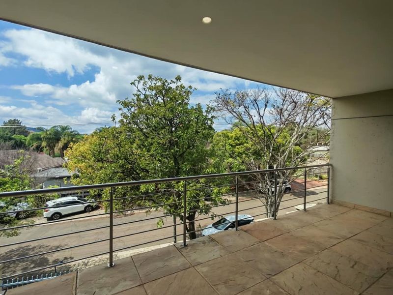 A spacious covered balcony featuring tiled flooring, a modern stainless steel balustrade, and recessed ceiling lighting, offering an elevated view of the street.