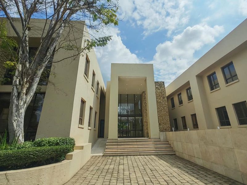 A modern commercial building entrance featuring stone cladding, a paved walkway, and a prominent glass facade with recessed lighting.
