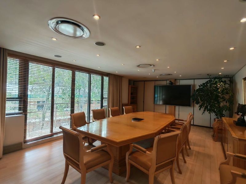 A professional boardroom featuring hardwood flooring, recessed lighting, and large windows with venetian blinds, providing a bright and functional workspace.