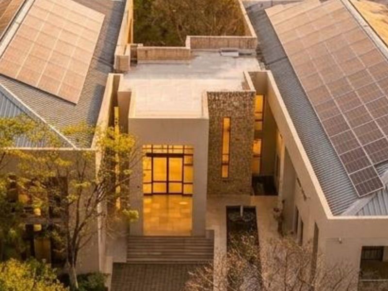 Aerial view of a modern commercial property featuring extensive solar panel installations, stone facade accents, and a central water feature at the main entrance.