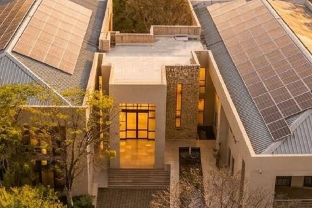 Aerial view of a modern commercial property featuring extensive solar panel installations, stone facade accents, and a central water feature at the main entrance.
