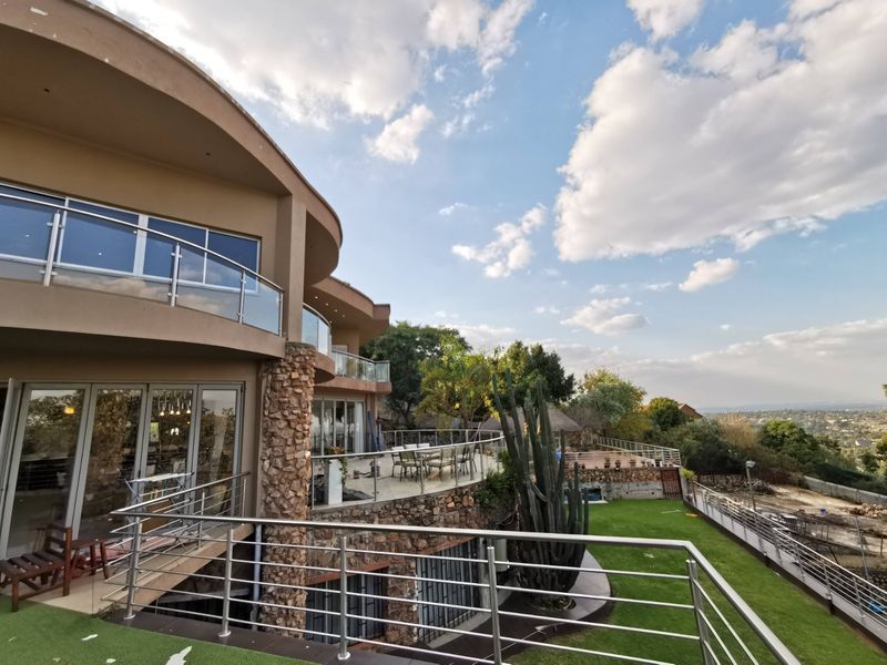 Spacious multi-level rear exterior featuring curved balconies with glass and stainless steel railings, stone accents, and expansive views over the landscaped garden.