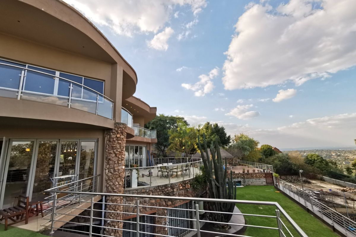 Spacious multi-level rear exterior featuring curved balconies with glass and stainless steel railings, stone accents, and expansive views over the landscaped garden.