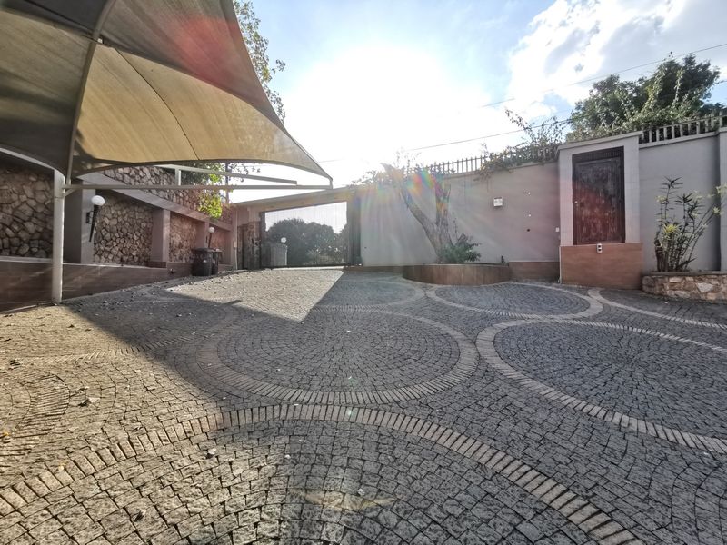 A paved driveway featuring a shade sail, stone-clad perimeter walls, and a secure entrance gate, providing a private and well-defined front access area.