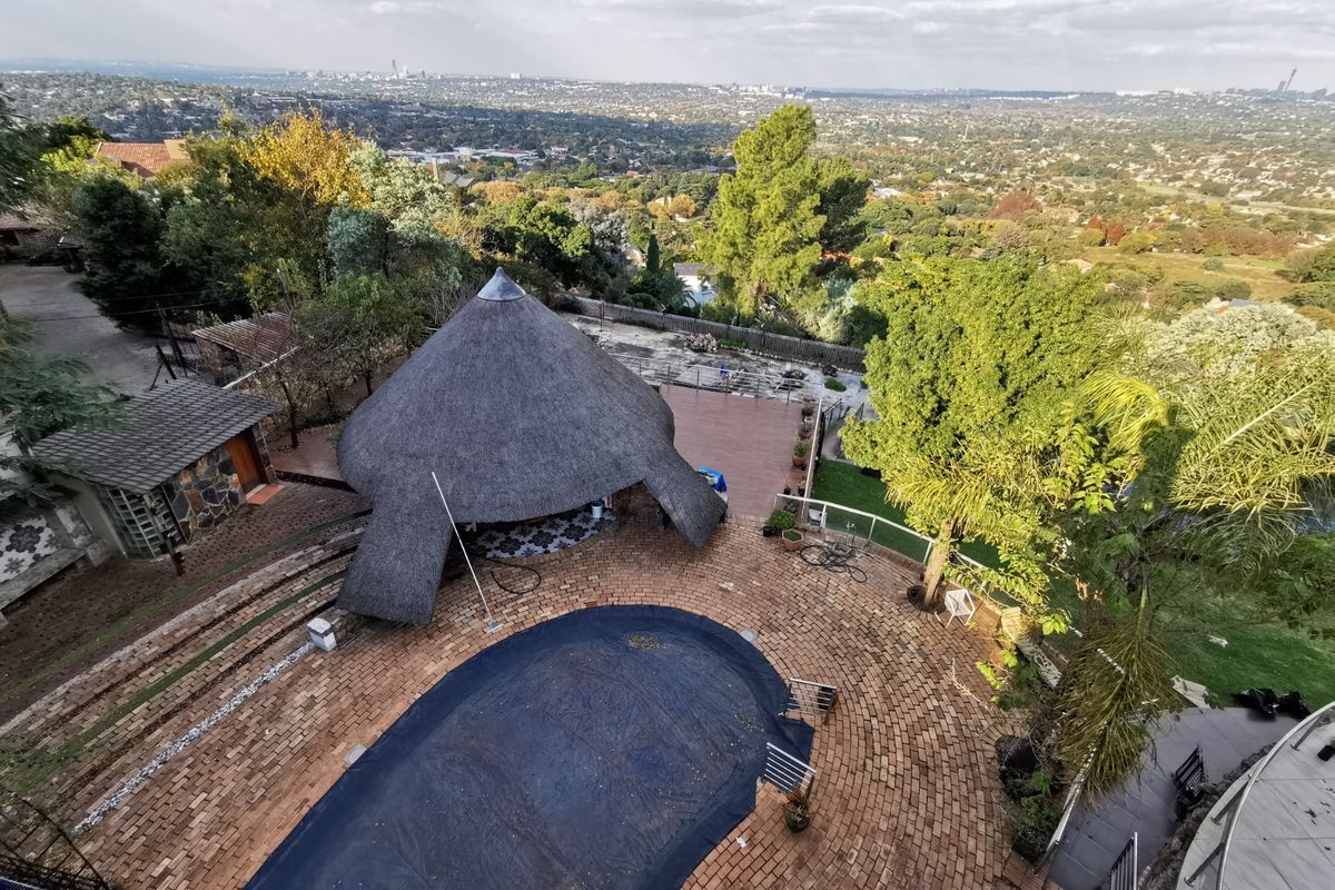 Aerial view of a property featuring a swimming pool, a traditional thatch roof lapa, and extensive paved outdoor entertainment areas with panoramic landscape views.