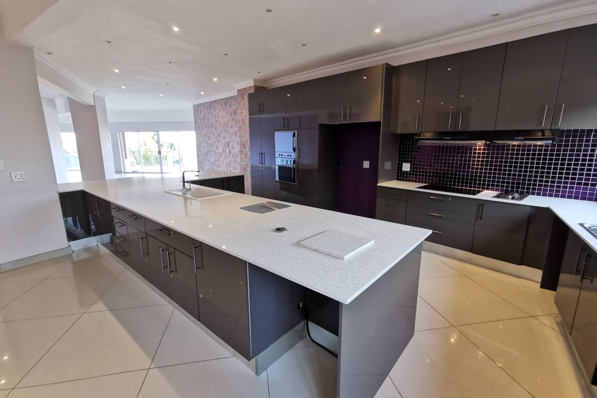 Modern, spacious kitchen featuring a large central island with quartz countertops, high-gloss cabinetry, built-in appliances, and a striking mosaic tile backsplash.