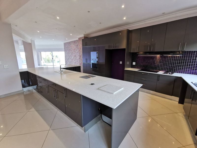 Modern, spacious kitchen featuring a large central island with quartz countertops, high-gloss cabinetry, built-in appliances, and a striking mosaic tile backsplash.