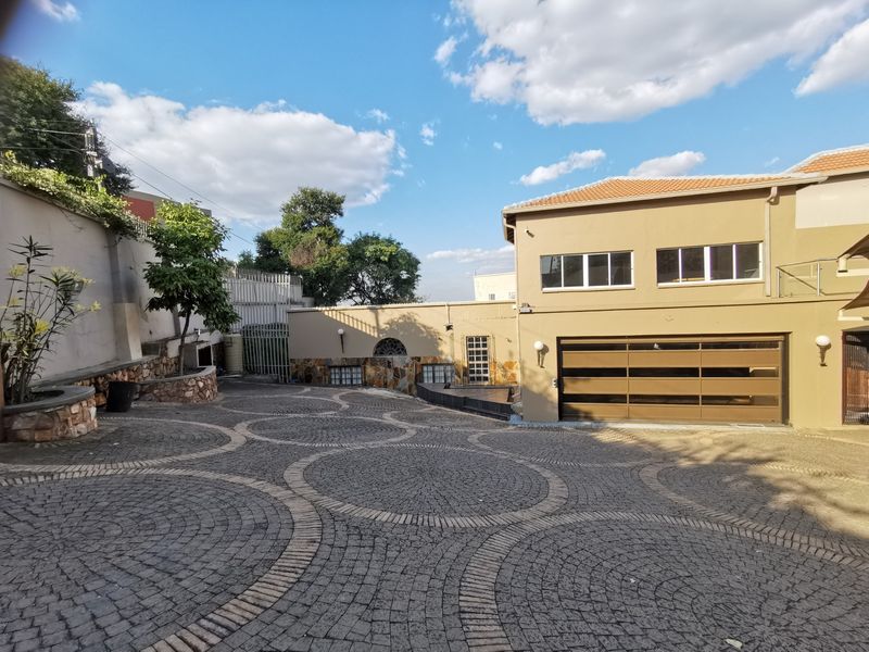 A well-maintained front exterior featuring a decorative circular pattern cobblestone driveway, stone-clad retaining walls, and a modern automated garage door.