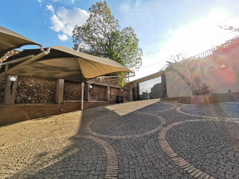 A paved driveway featuring decorative cobblestone patterns, a large shade sail structure, and stone-clad perimeter walls with a secure entrance gate.
