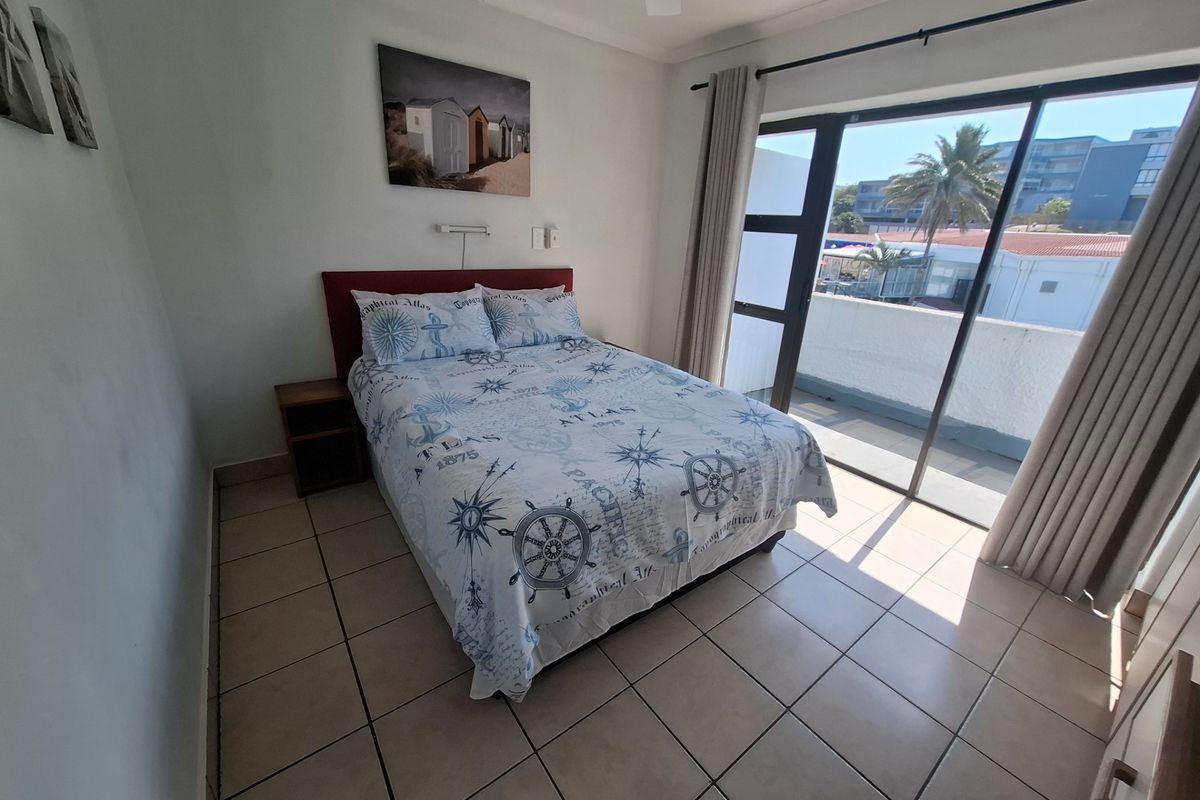 A bedroom featuring tiled flooring and a large sliding glass door providing access to a balcony with natural light.