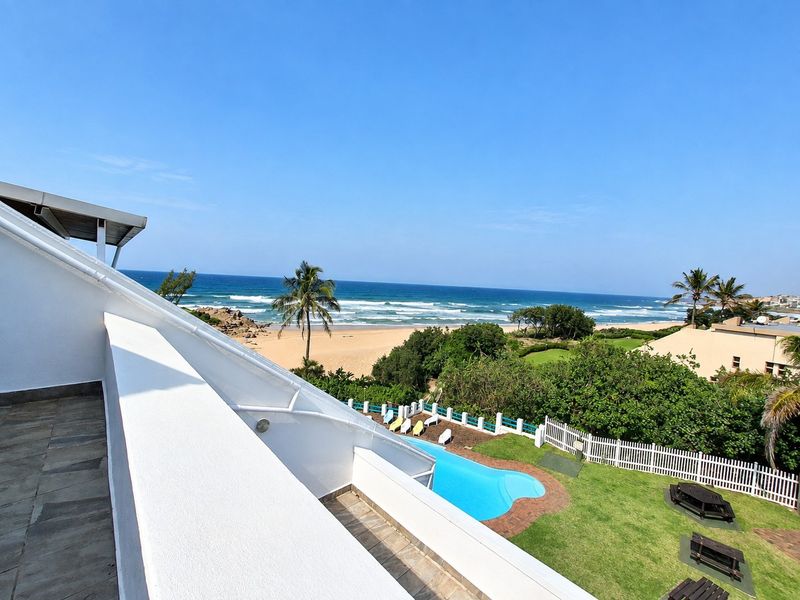 Elevated view overlooking a swimming pool, landscaped garden, and direct beach access with ocean vistas.