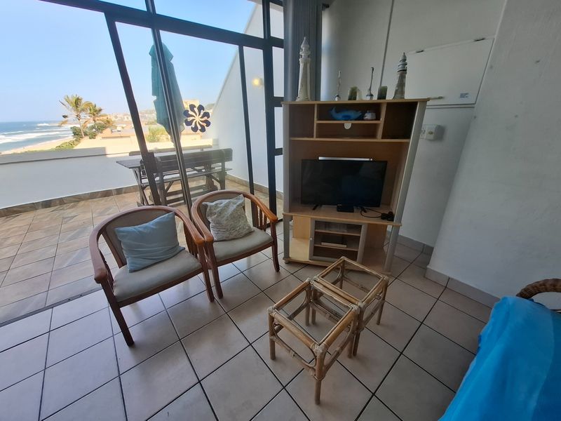 A living area featuring tiled flooring and large sliding glass doors that provide access to a balcony with ocean views.
