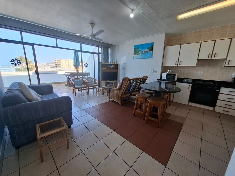 Open-plan living and kitchen area featuring tiled floors, built-in cabinetry, and large sliding doors leading to a balcony with ocean views.
