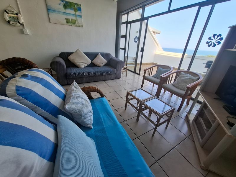 A living room featuring tiled flooring and large sliding glass doors that provide access to a balcony with ocean views.