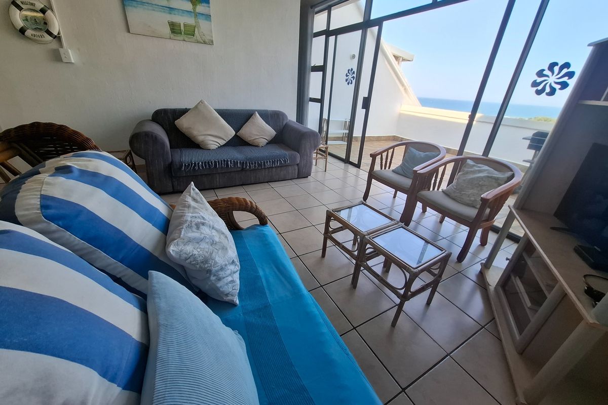 A living room featuring tiled flooring and large sliding glass doors that provide access to a balcony with ocean views.
