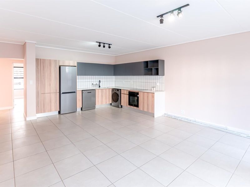 Modern open-plan kitchen featuring light wood and dark grey cabinetry, tiled flooring, integrated oven, and clean white tiled backsplash in a bright, spacious layout.