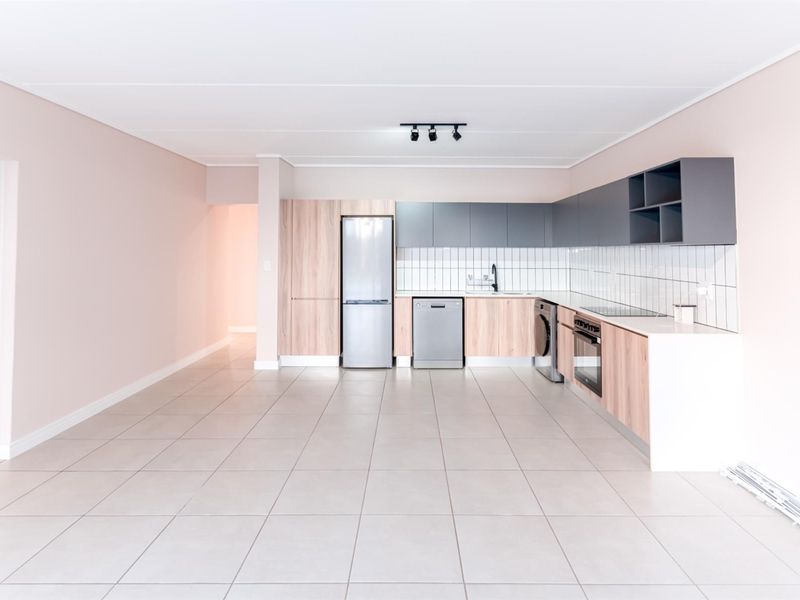 Modern, open-plan kitchen featuring sleek two-tone cabinetry, tiled backsplash, integrated appliances, and neutral tiled flooring in a clean, well-maintained space.