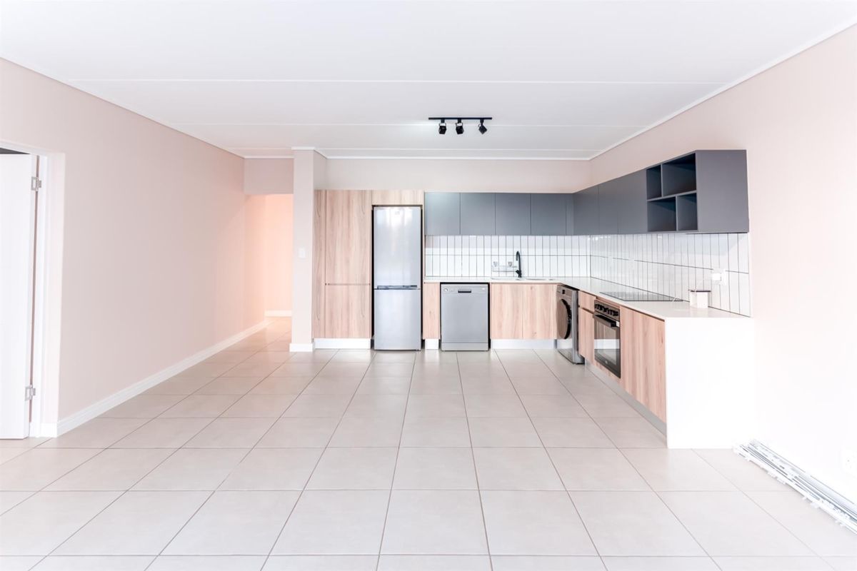 Modern, open-plan kitchen featuring sleek two-tone cabinetry, tiled backsplash, integrated appliances, and neutral tiled flooring in a clean, well-maintained space.