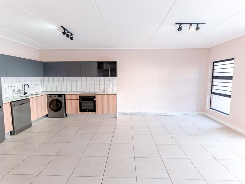 Modern open-plan kitchen featuring light wood and grey cabinetry, tiled flooring, built-in oven, and hob, offering a clean and functional living space.