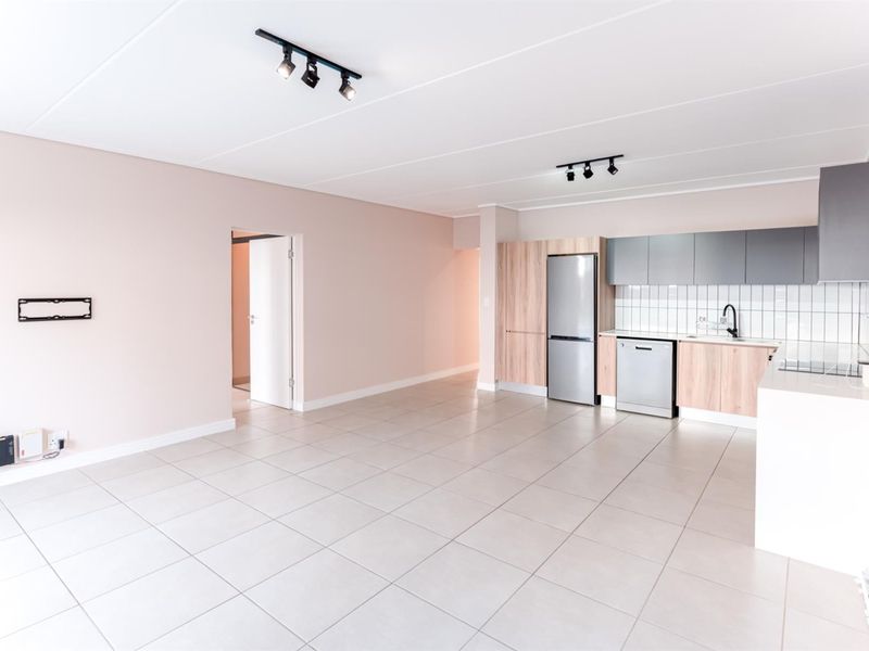 A bright, open-plan living and kitchen area featuring modern cabinetry, tiled flooring, and contemporary track lighting in a clean, well-maintained space.