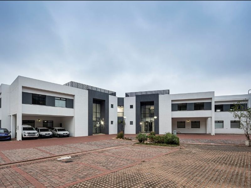 Modern office building exterior featuring a paved driveway, covered parking bays, and a clean, contemporary facade with glass entrance points.