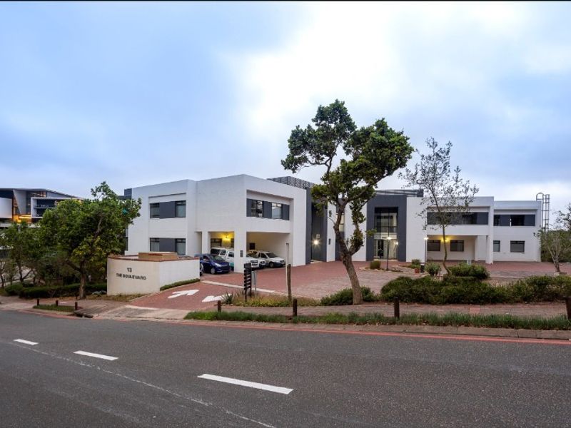 Front exterior view of a modern office building featuring a paved driveway, covered parking bays, and well-maintained landscaped grounds.