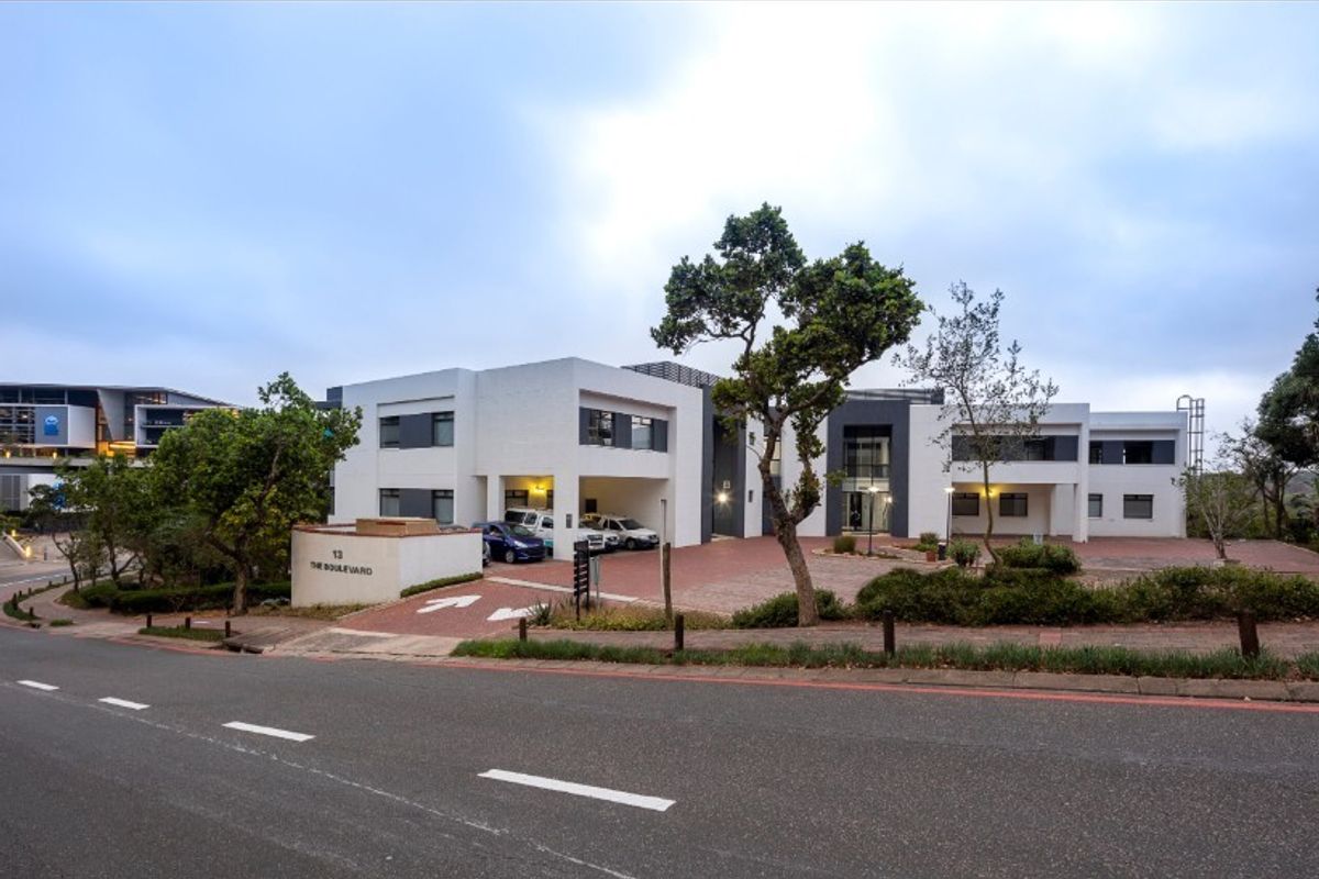 Front exterior view of a modern office building featuring a paved driveway, covered parking bays, and well-maintained landscaped grounds.