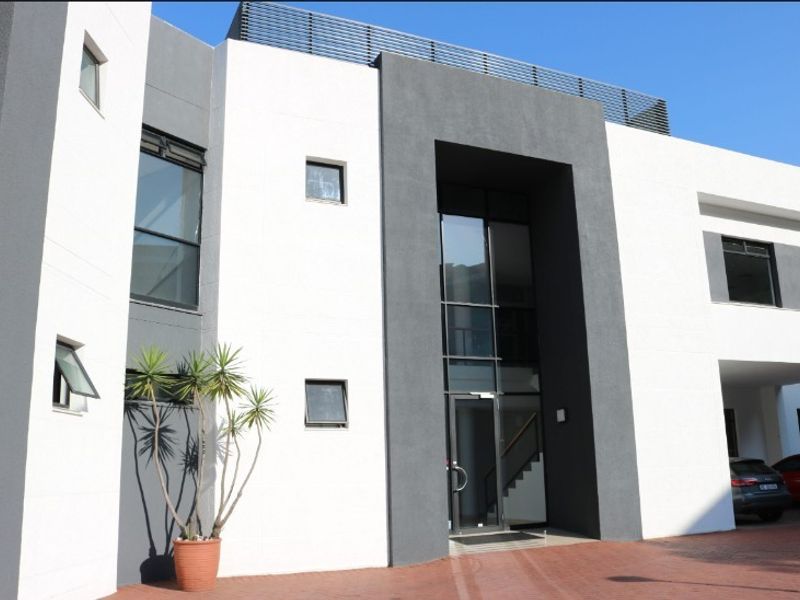 Modern office building exterior featuring a contemporary two-tone facade, large glass entrance, and paved driveway access.