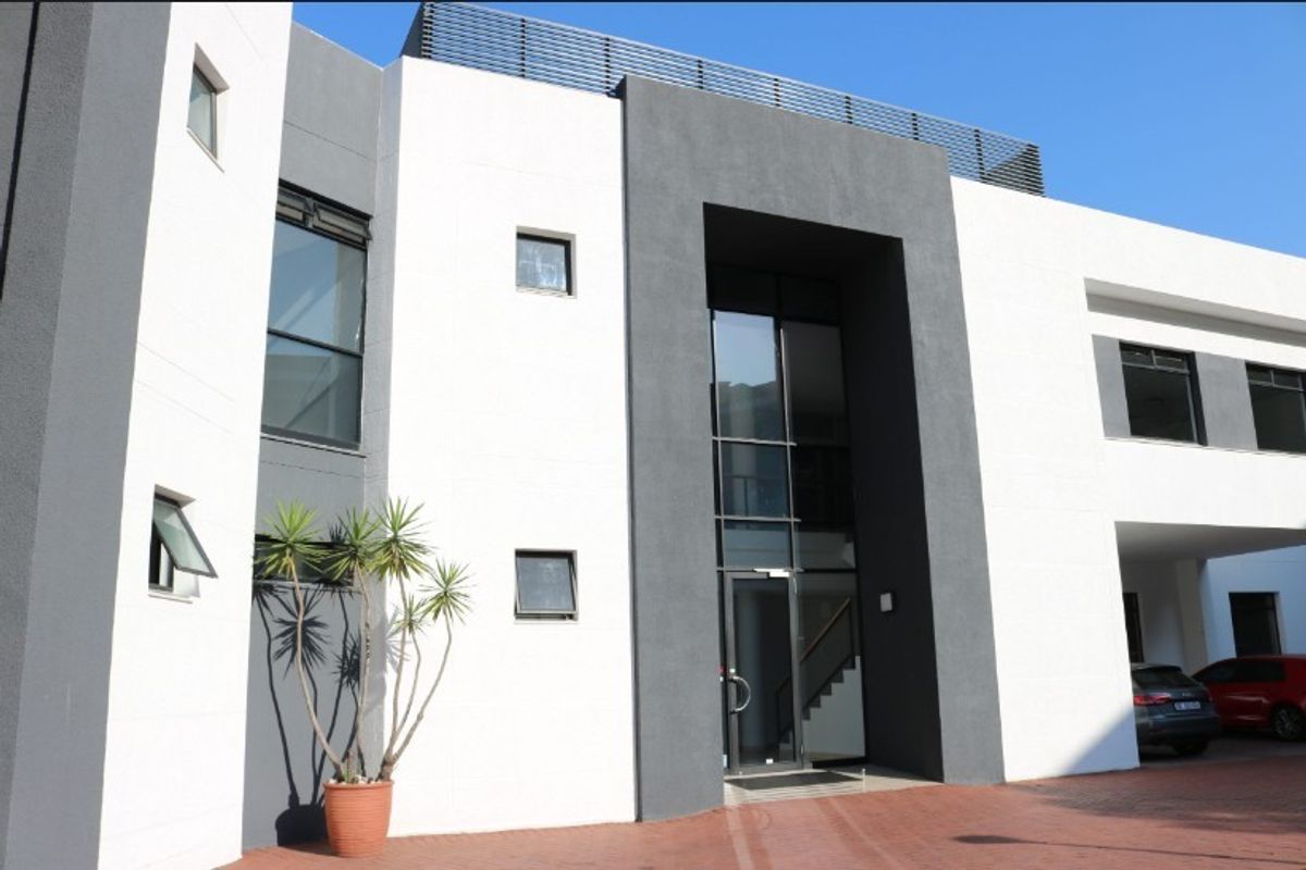 Modern office building exterior featuring a contemporary two-tone facade, large glass entrance, and paved driveway access.