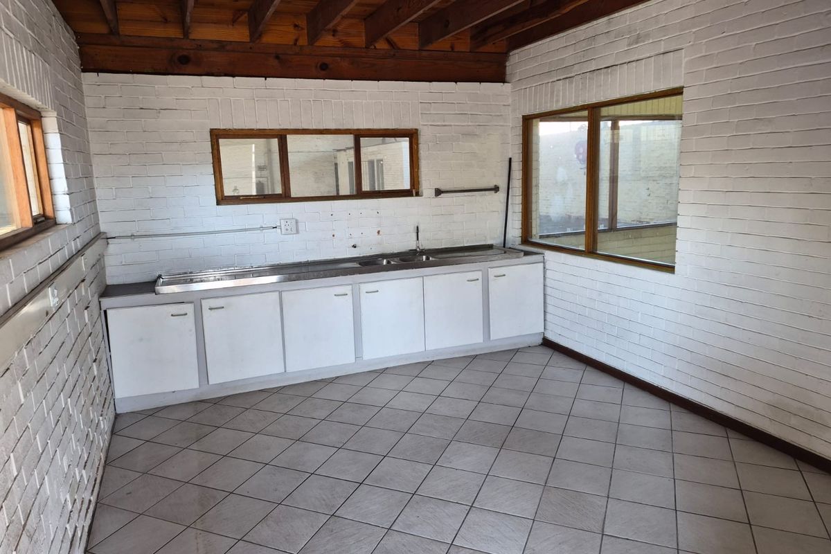A functional industrial-style kitchen area featuring exposed timber ceiling beams, painted brick walls, tiled flooring, and a built-in stainless steel sink unit.