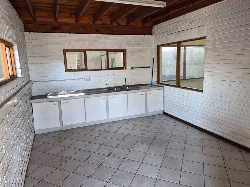 A functional industrial-style kitchen area featuring exposed timber ceiling beams, painted brick walls, tiled flooring, and a built-in stainless steel sink unit.